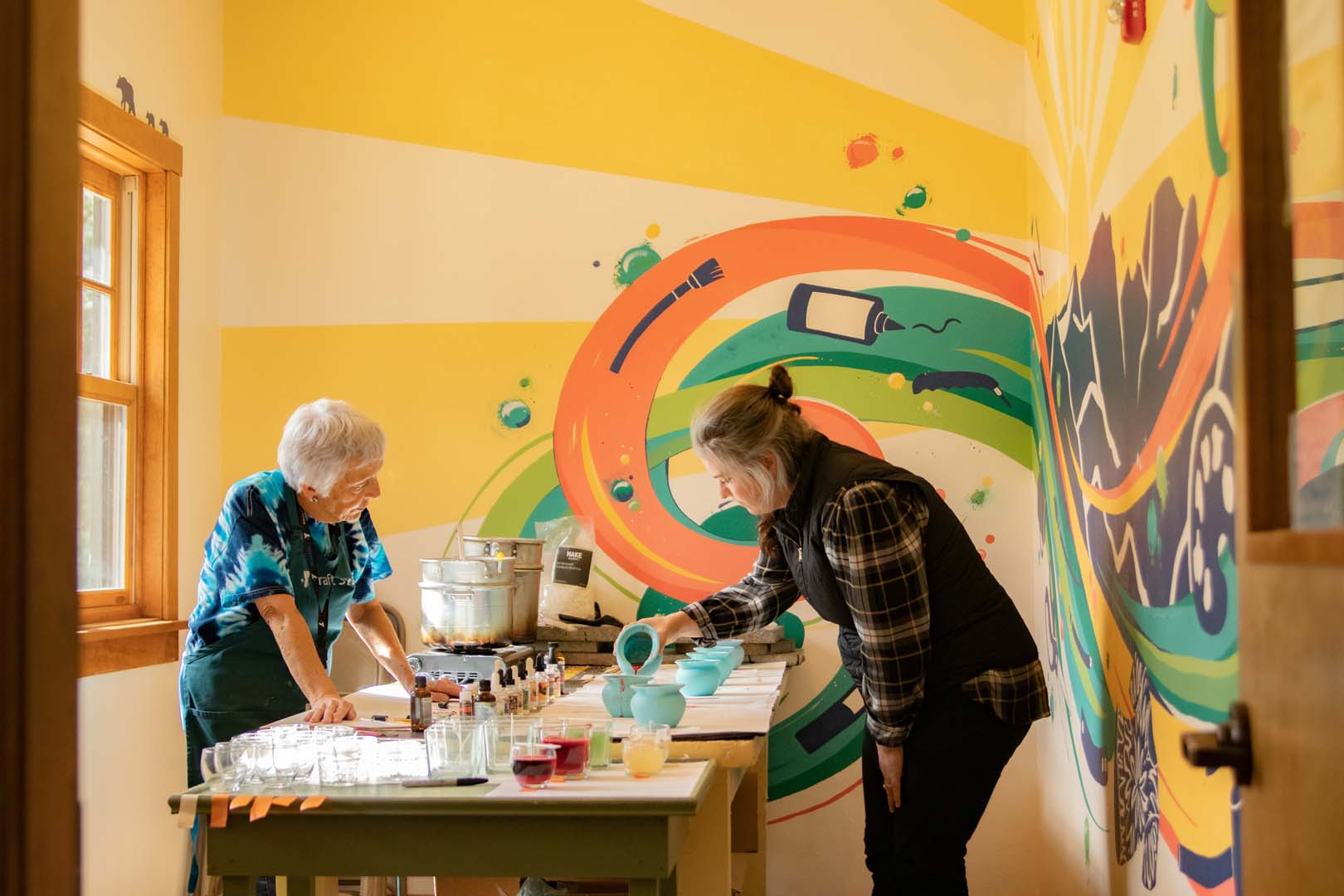 Two women in craft shop painting some small pots blue and red