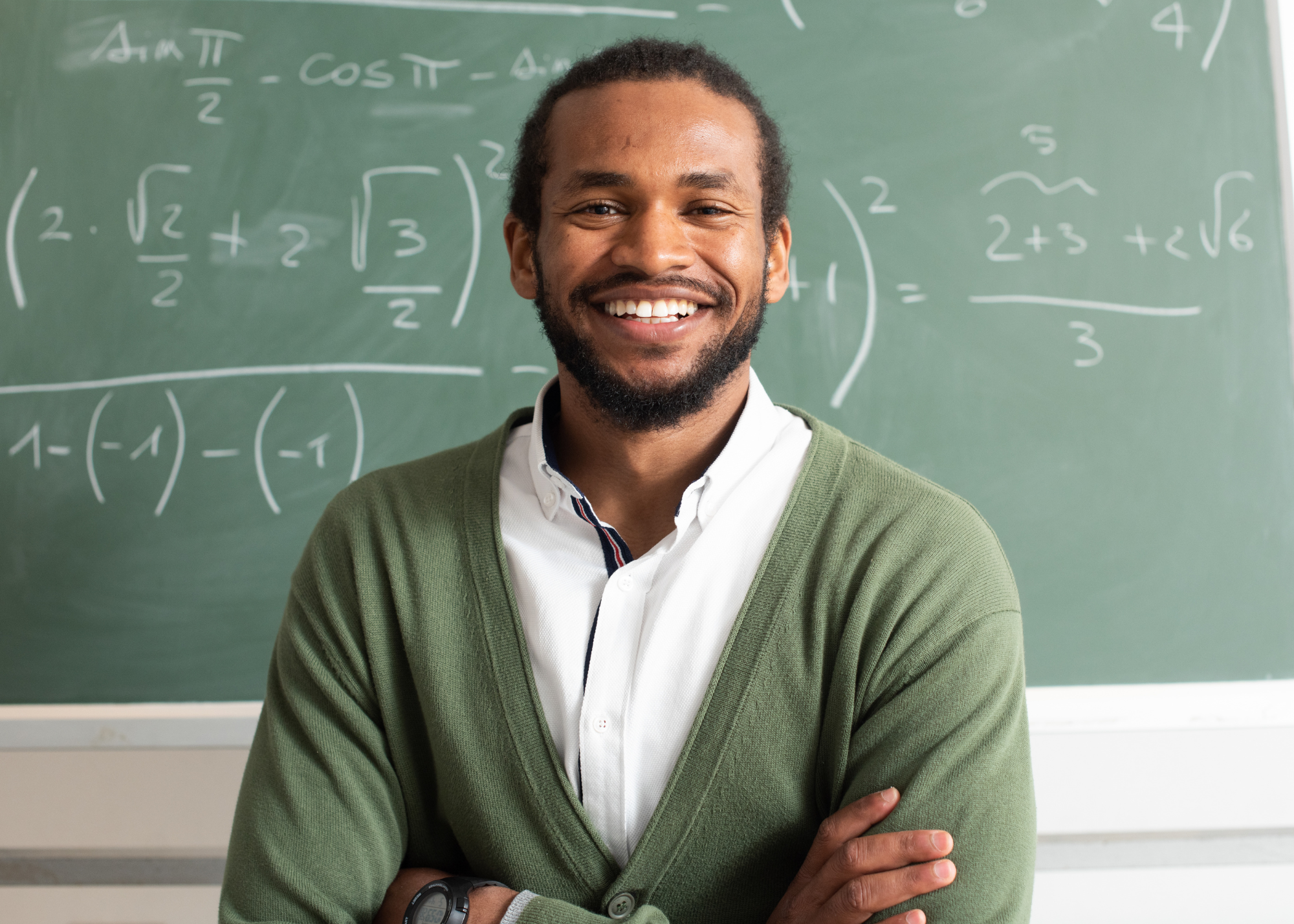 Male teacher with arms crossed in front of chalkboard smiling
