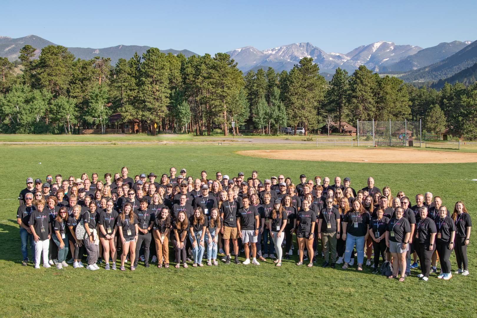 Large group outside in baseball diamond with mountains in the background