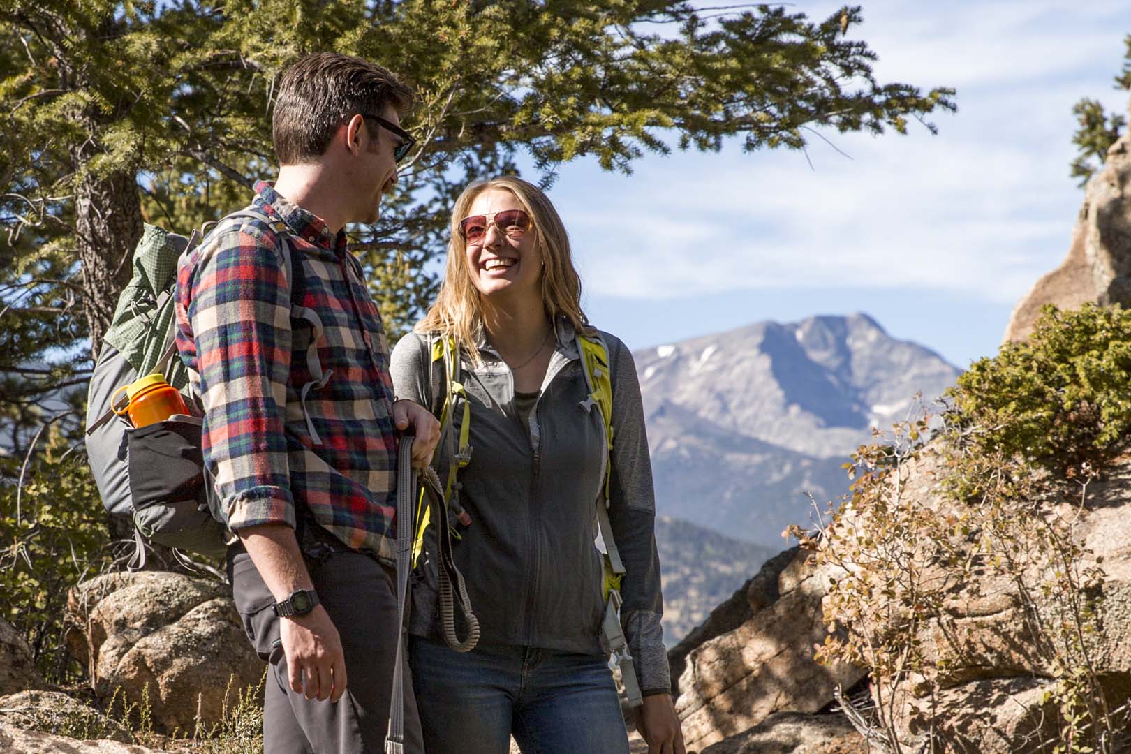 Hombre y mujer en una caminata con árboles y montañas al fondo