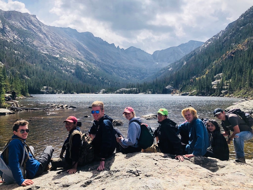 Grupo de personas sentadas junto a un lago con montañas al fondo