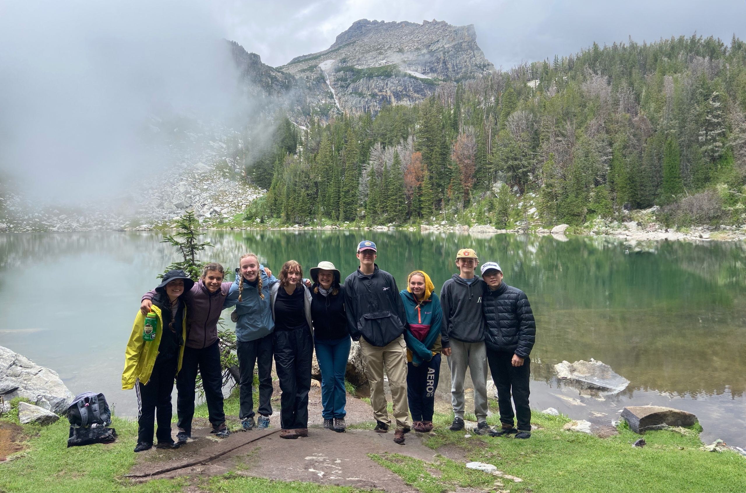 group gathered by the water with mountains in the background