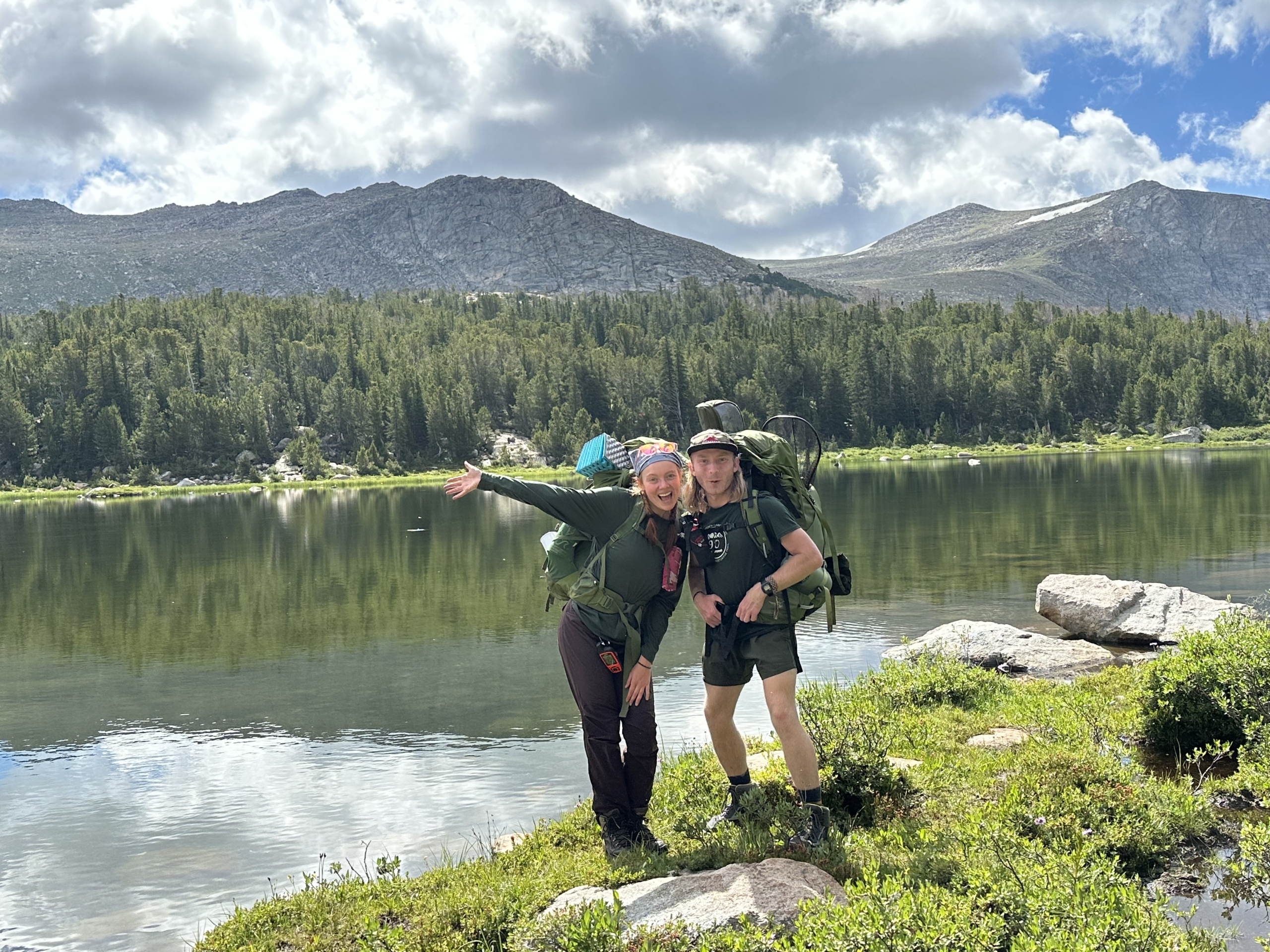 two people standing in front of water and mountains