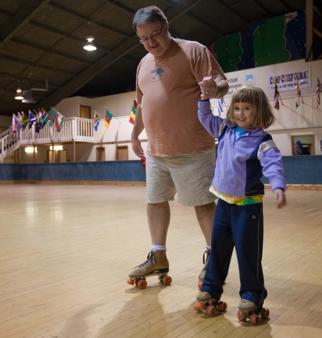 Little girl roller skating with help from a man