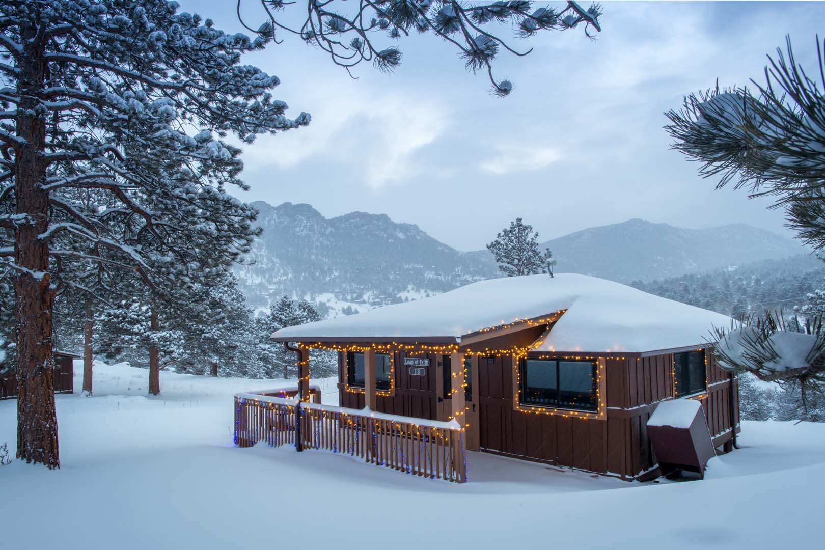 cabin with snow on top of it with mountain in the background