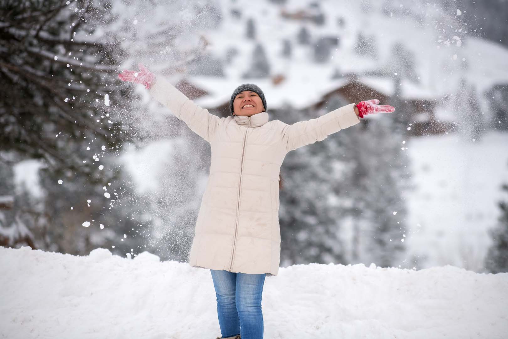 Woman throwing snow into the air with trees behind her