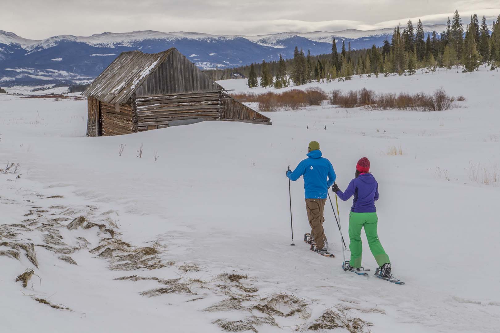 People cross country skiing near a cabin with mountains in background
