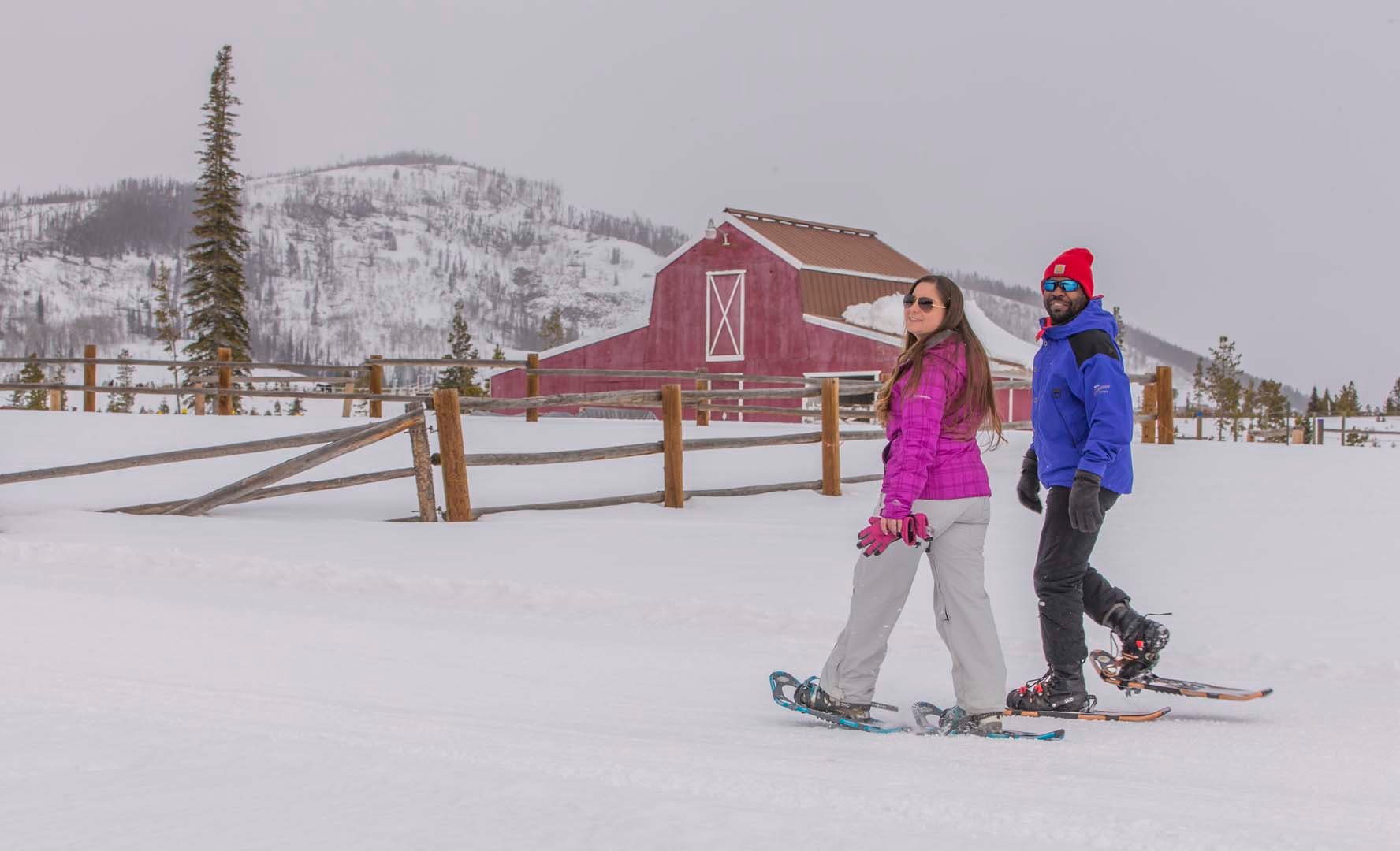 People snowshoeing near a farm with mountains in the background