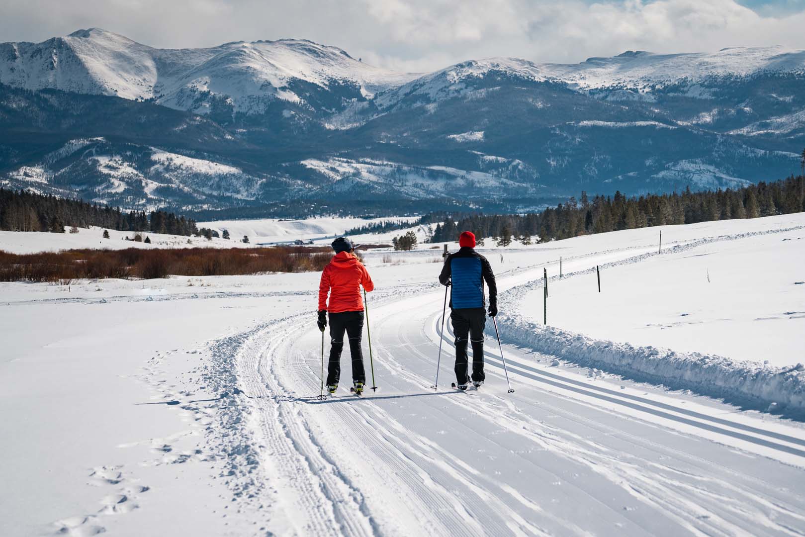Two people cross country skiing with mountains in background