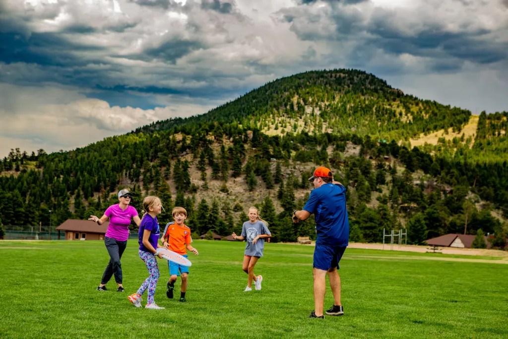 Niños jugando al frisbee en el césped con las Montañas Rocosas al fondo.