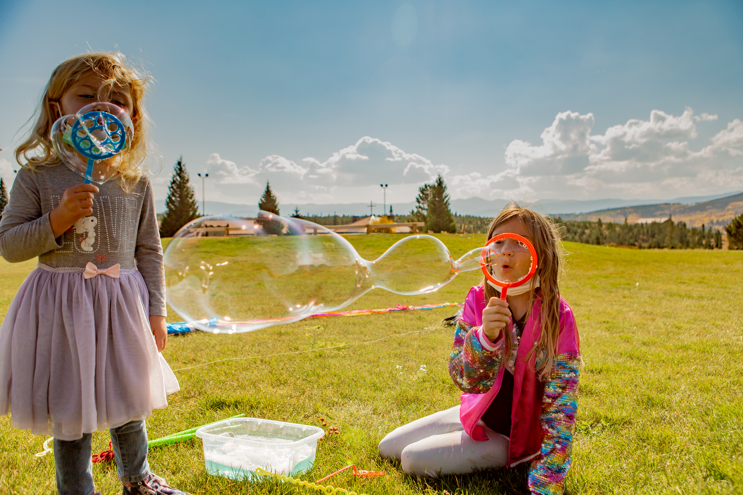 2 children blowing bubbles in field of grass